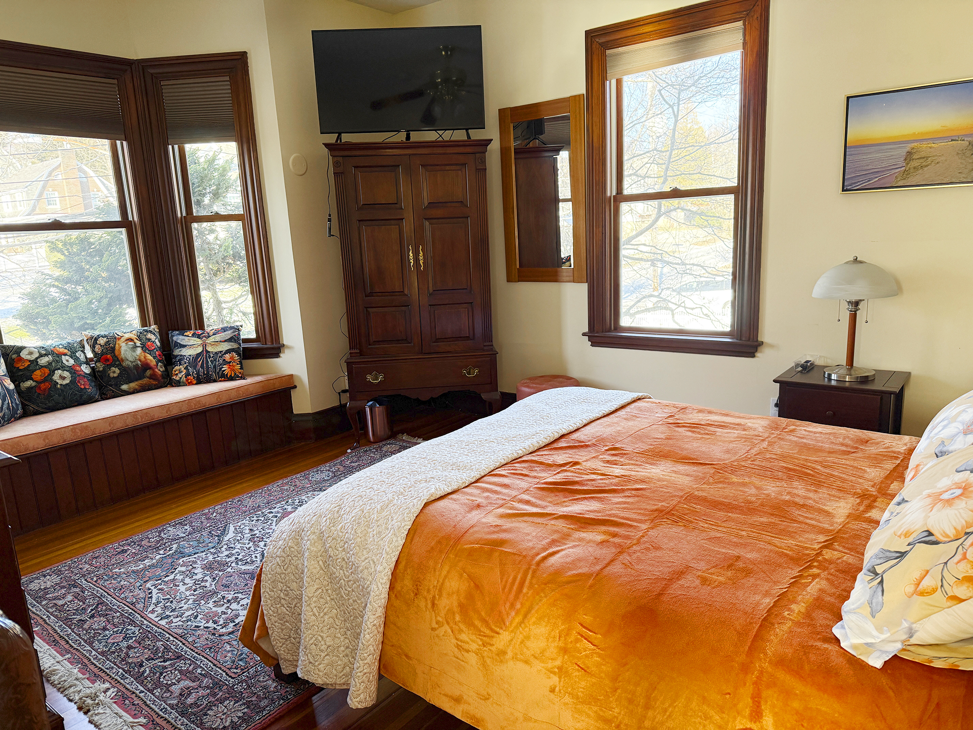 Cozy bedroom with an orange bedspread, windows, wooden furniture, and a small reading nook.