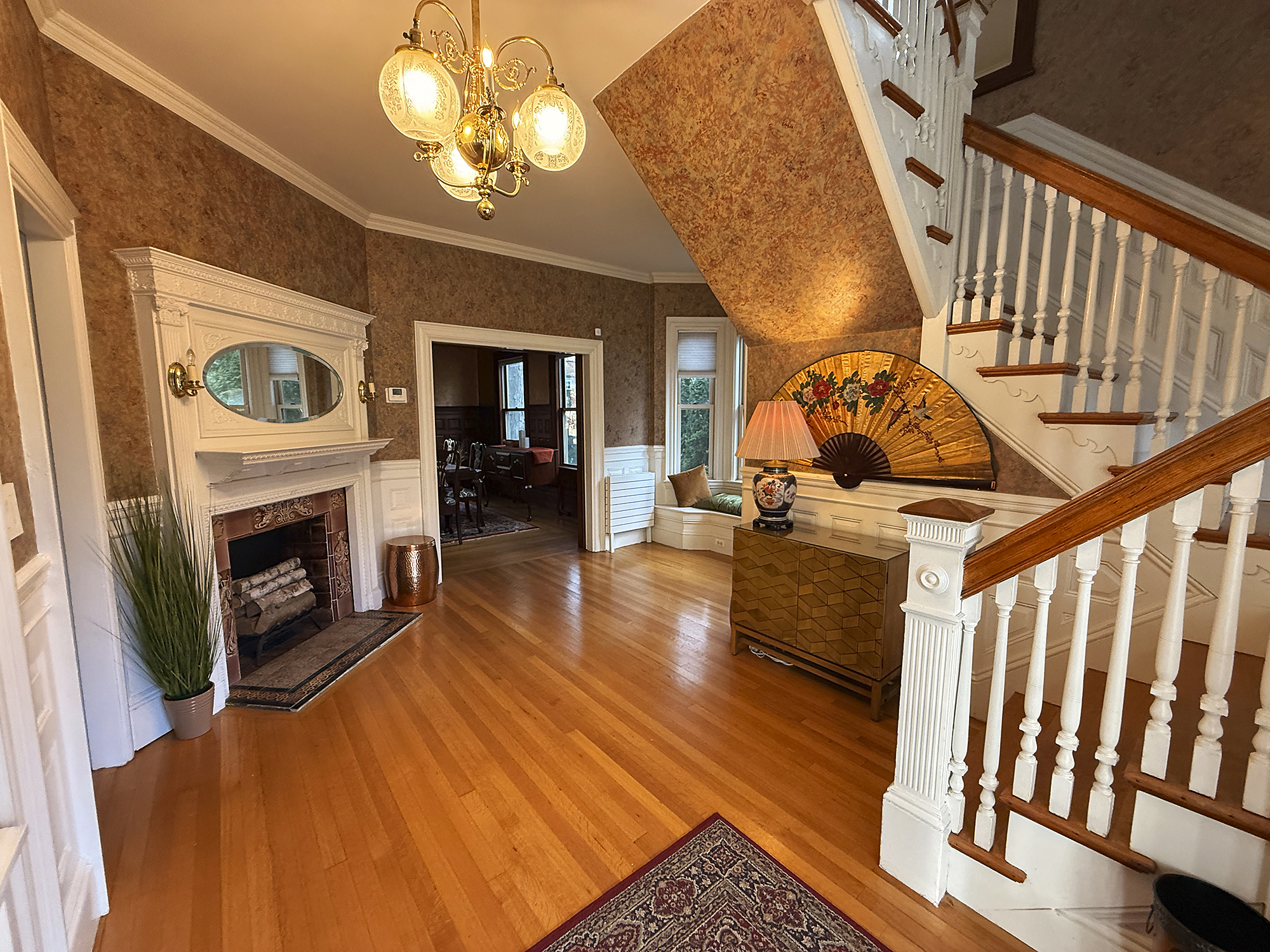 Elegant foyer with wooden staircase, decorative lamp, and vintage wallpaper.