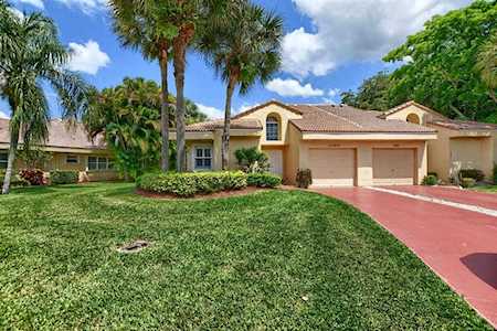 A cream colored, stone house with a terra cotta tiled roof, a big green lawn in front and palm trees in the yard.