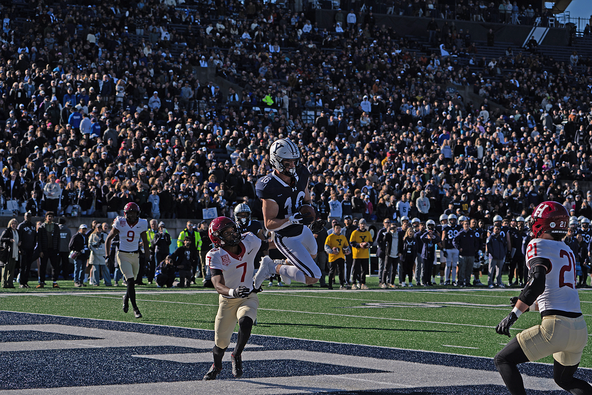 Yale player jumping in the air with ball in hands with Harvard player in pursuit