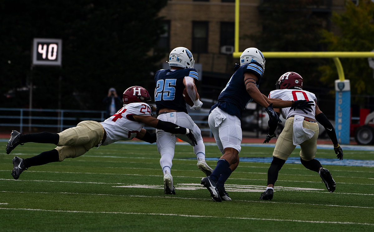 Columbia player has the ball and a Harvard player tackles Columbia player
