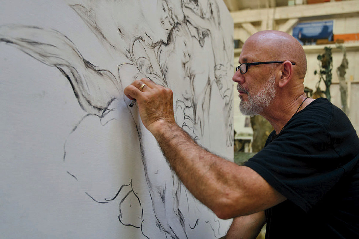 A man in glasses sketching a black and white image on a giant canvas.