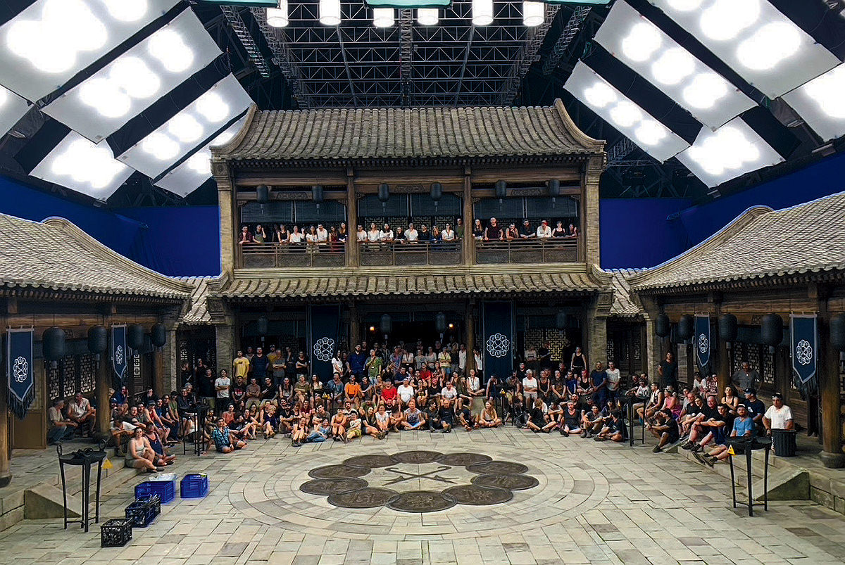 Dozens of people pose for a photo inside a large pagoda on a film set.