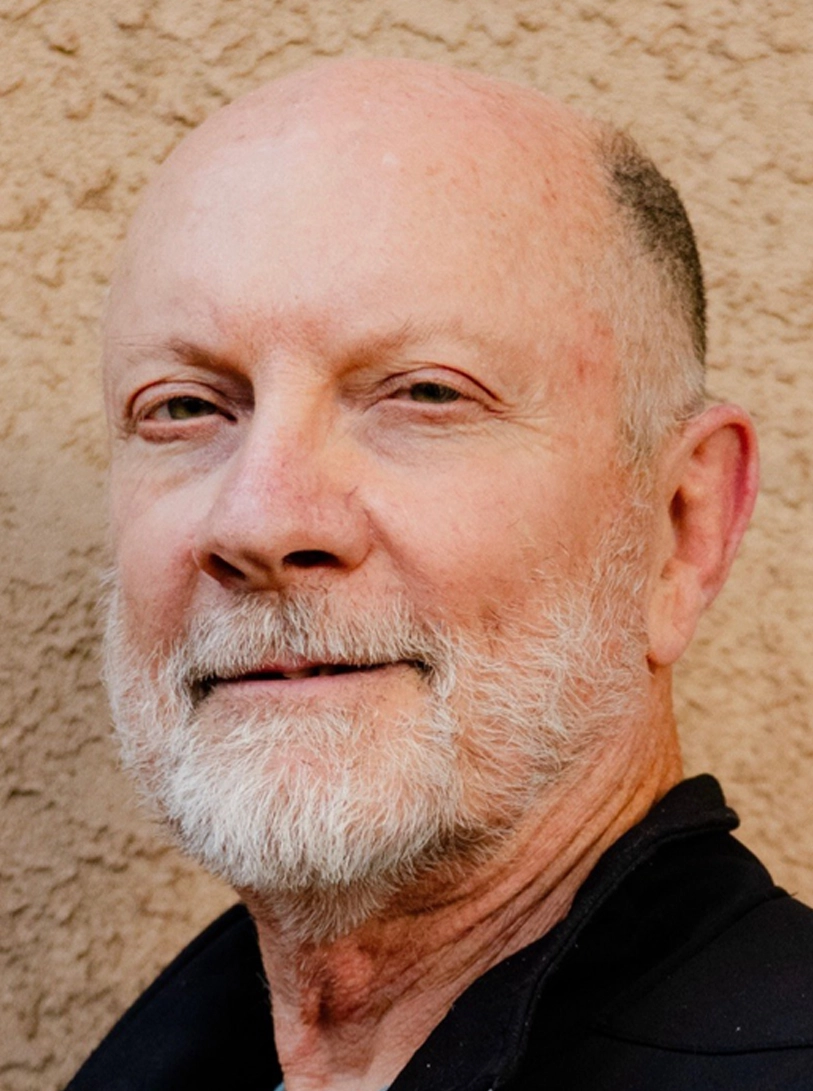 man with white beard, slight smile, against textured beige wall