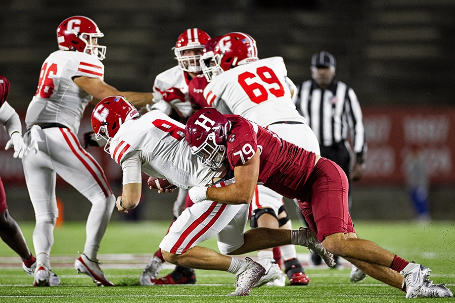 Harvard defender tackles Cornell quarterback mid-play under stadium lights.