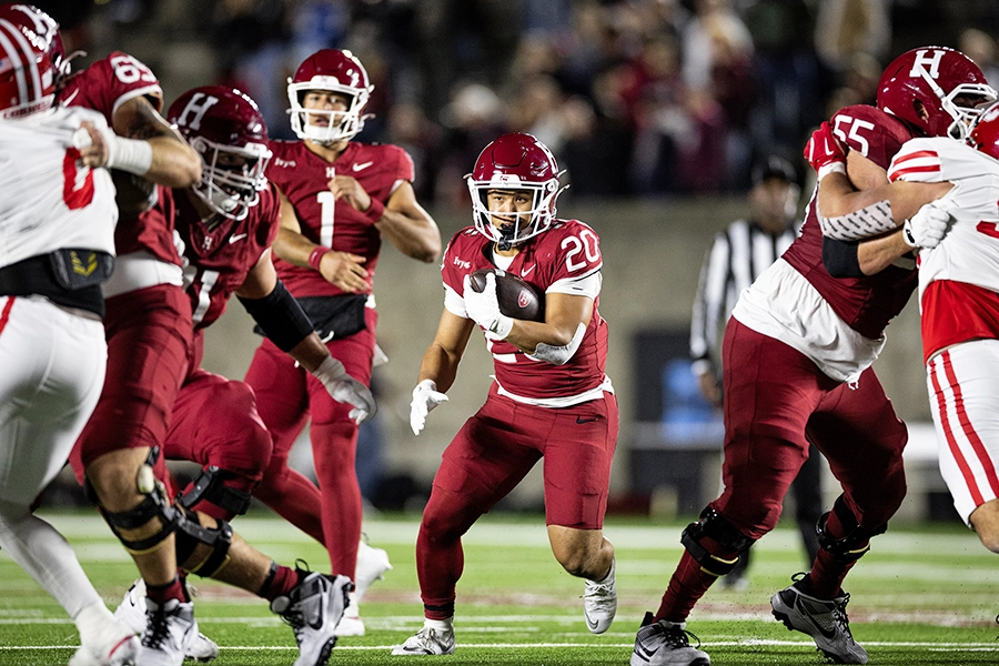 Harvard running back holds the ball, scanning for a gap in Cornell’s defense.