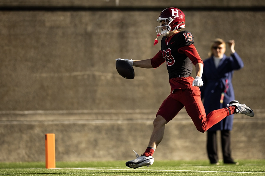 Harvard player #19 runs into the end zone holding a football, celebrating a touchdown.
