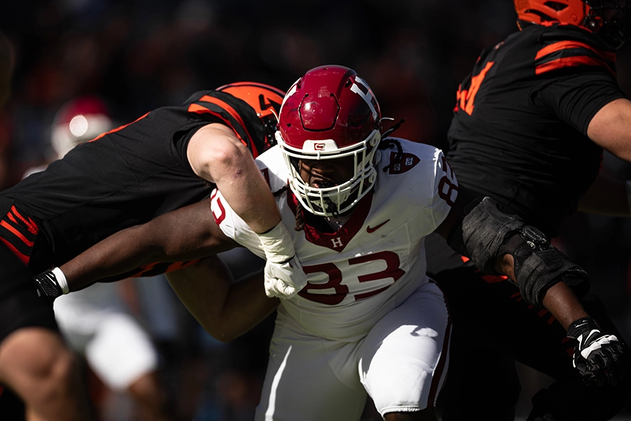 Harvard player battles through two Princeton defenders while advancing with the ball.