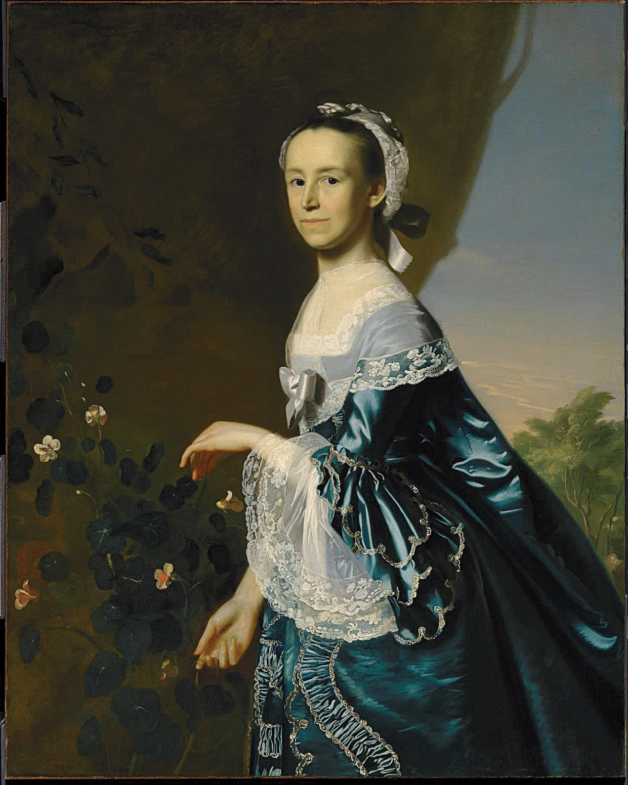 Painted portrait of Mercy Otis Warren showing her in an outdoor scene with trees and flowers and her wearing a lace bonnet and a blue satin gown with white lace accents
