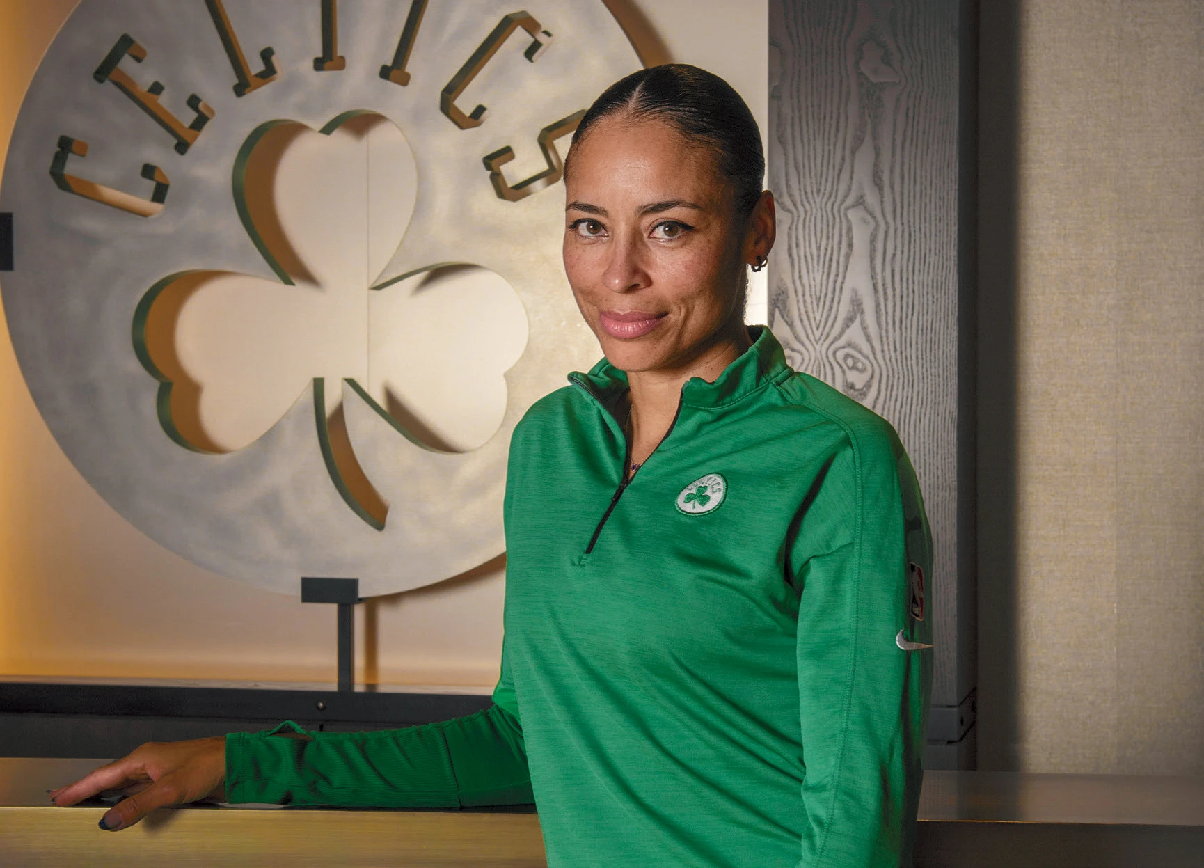 Woman with green jersey standing in front of sign for the Celtics