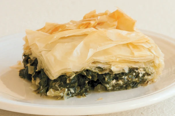 A dish consisting of puff pastry and cooked wild greens on a white plate