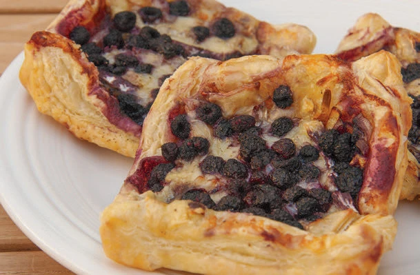 Three pastries with purple berries on them on a white plate