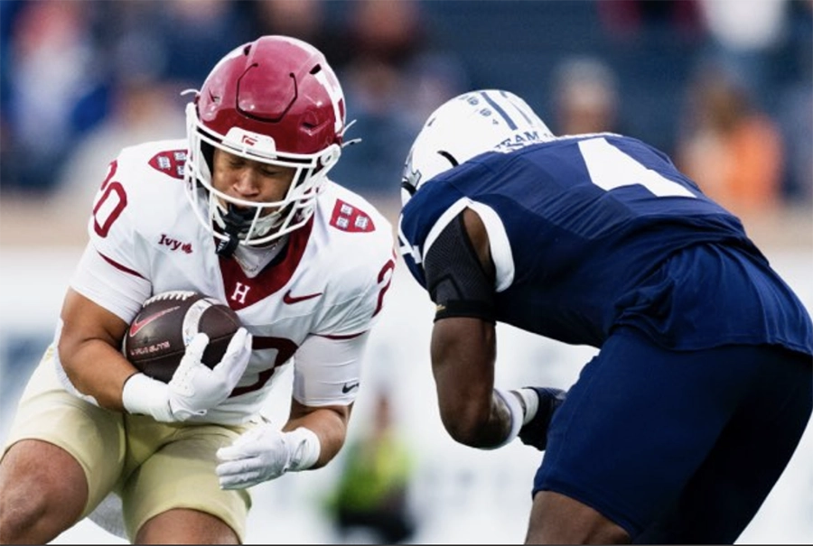 Harvard running back clutches the ball while being tackled by a Yale defender.