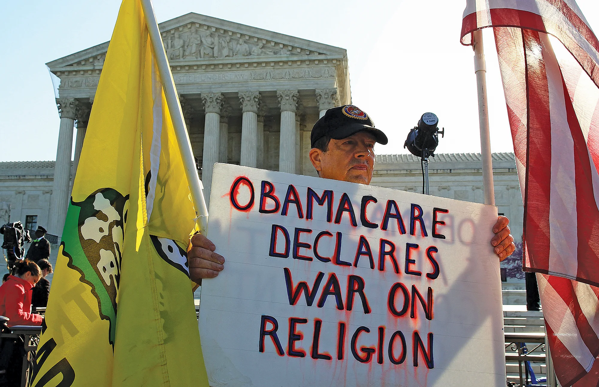 Person holding sign reading "Obamacare declares war on religion" outside Supreme Court.