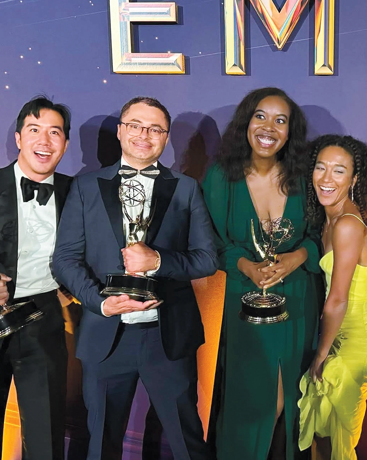 Four people dressed formally, holding Emmy awards and smiling in front of an award show backdrop.