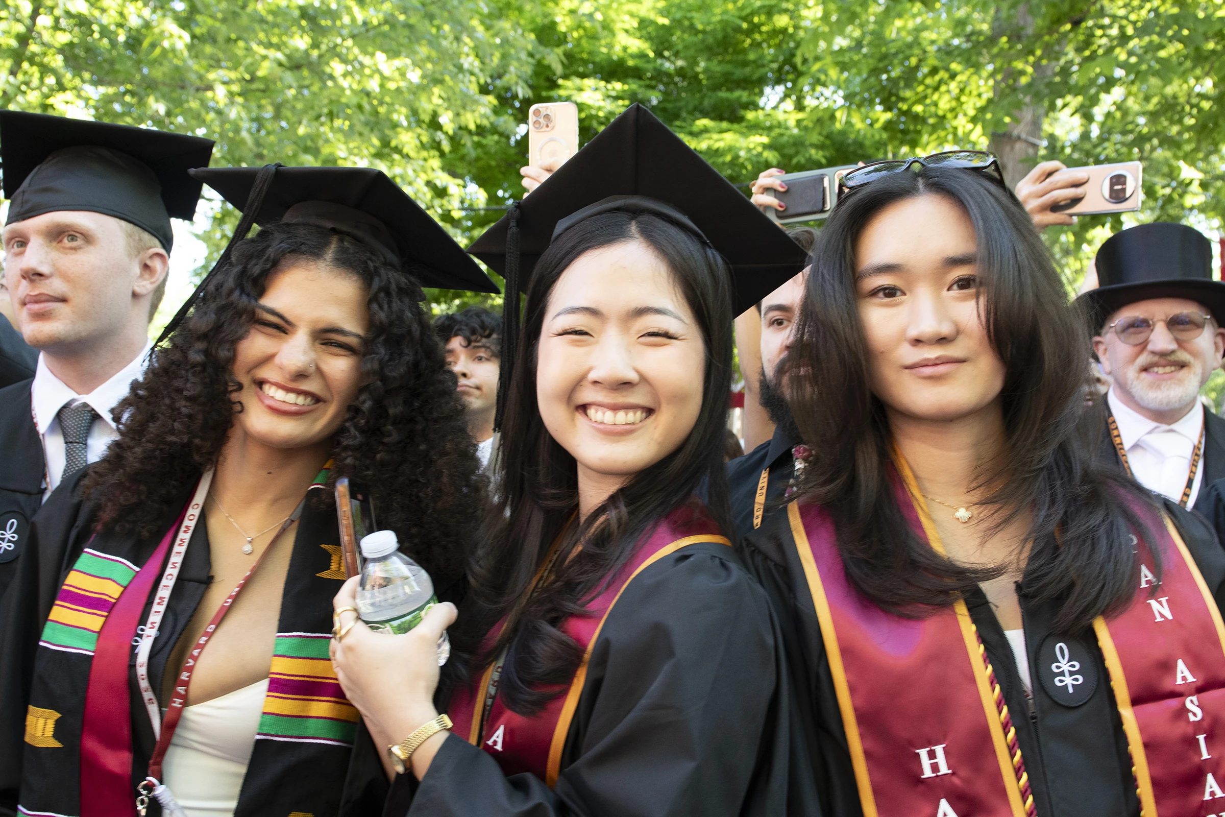 Students in graduation caps and gowns and red stoles smile in front of trees