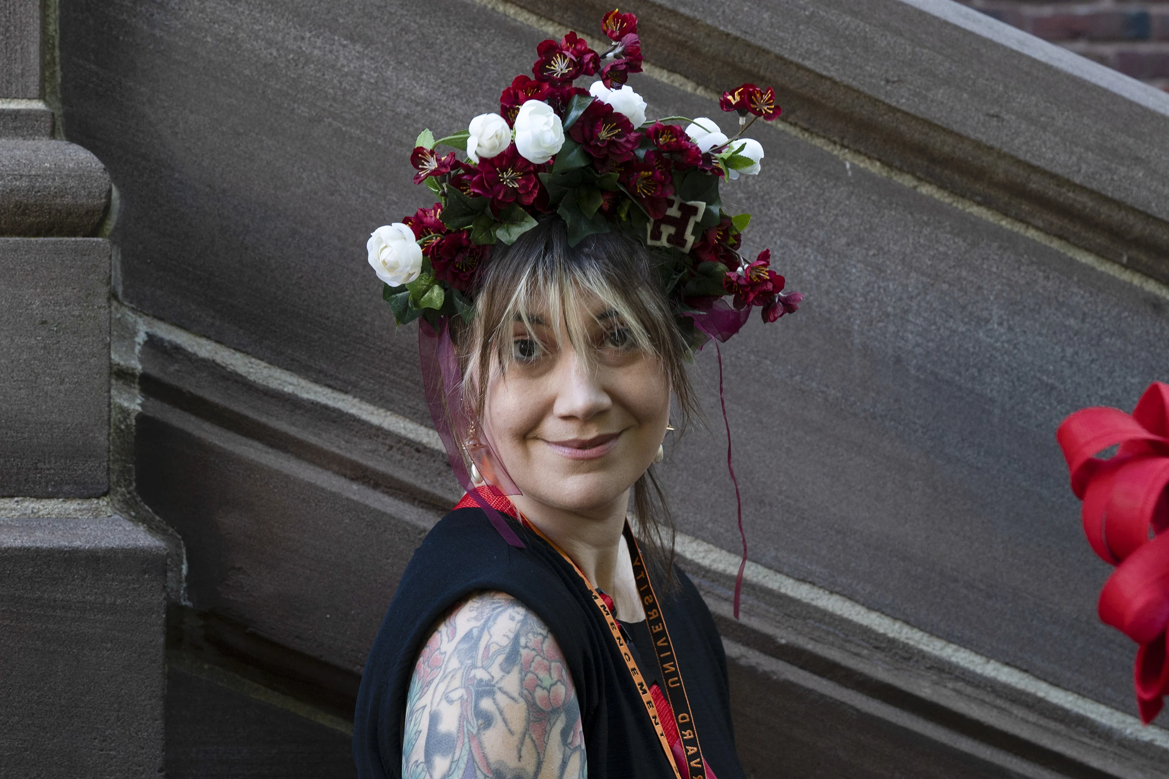 Woman with tattoos and black tank top wearing a flower crown with white and red flowers