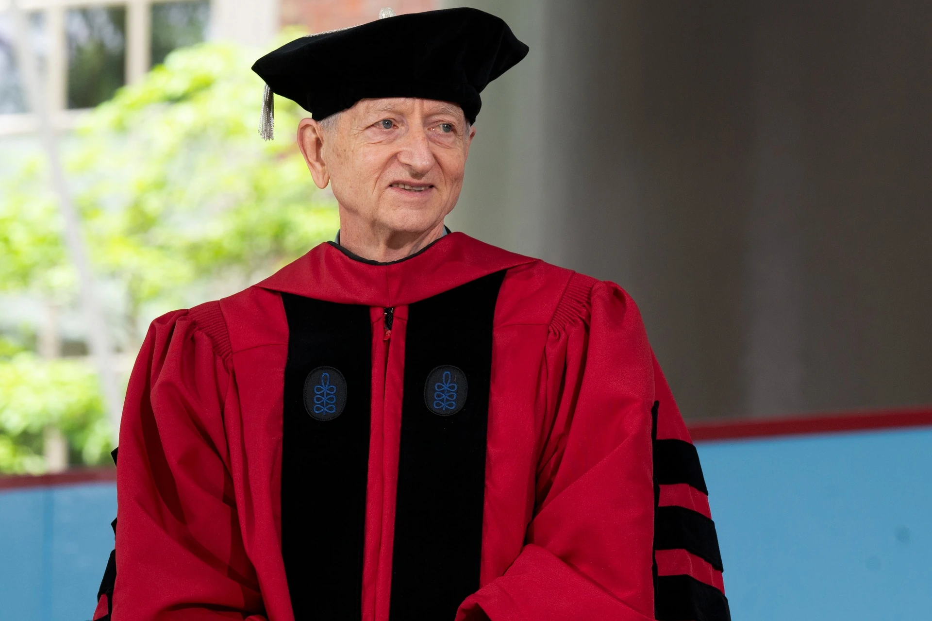 Geoffrey Hinton wearing red doctoral robe stands on a stage