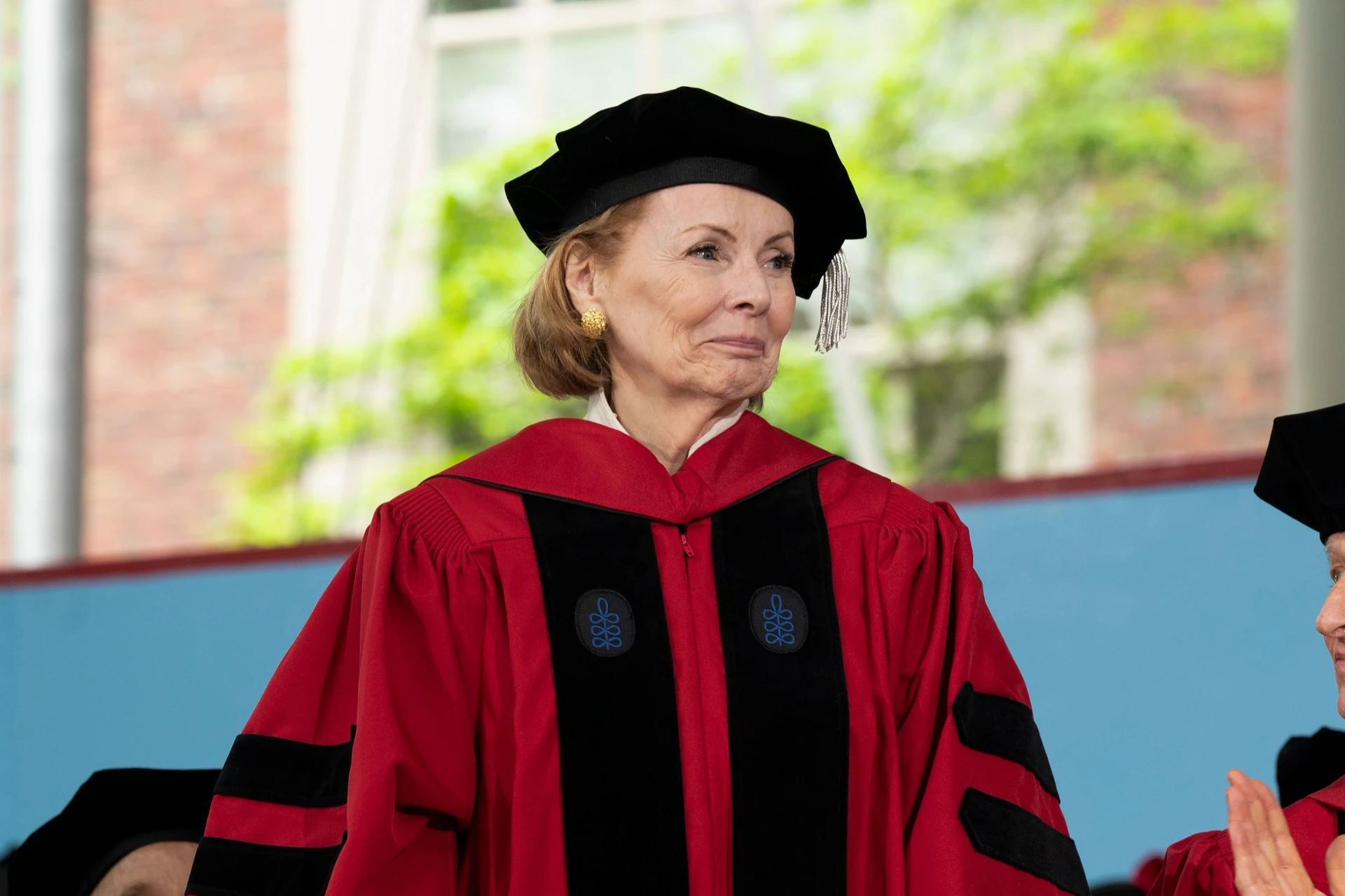 Peggy Noonan smiles while wearing a red doctoral robe on a stage