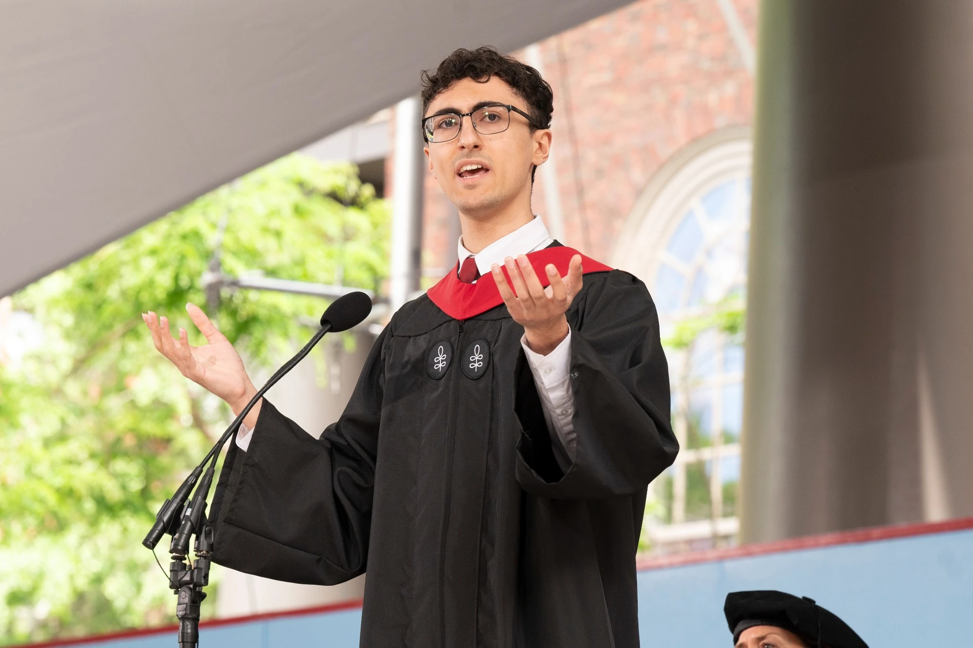 Young man wearing black robe speaking on a stage