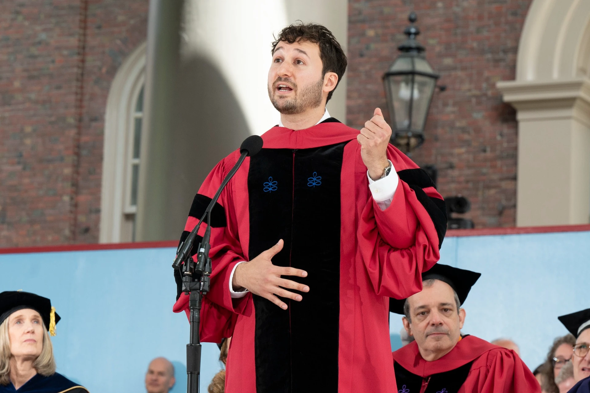 Young man wearing red graduate robe speaking on a stage