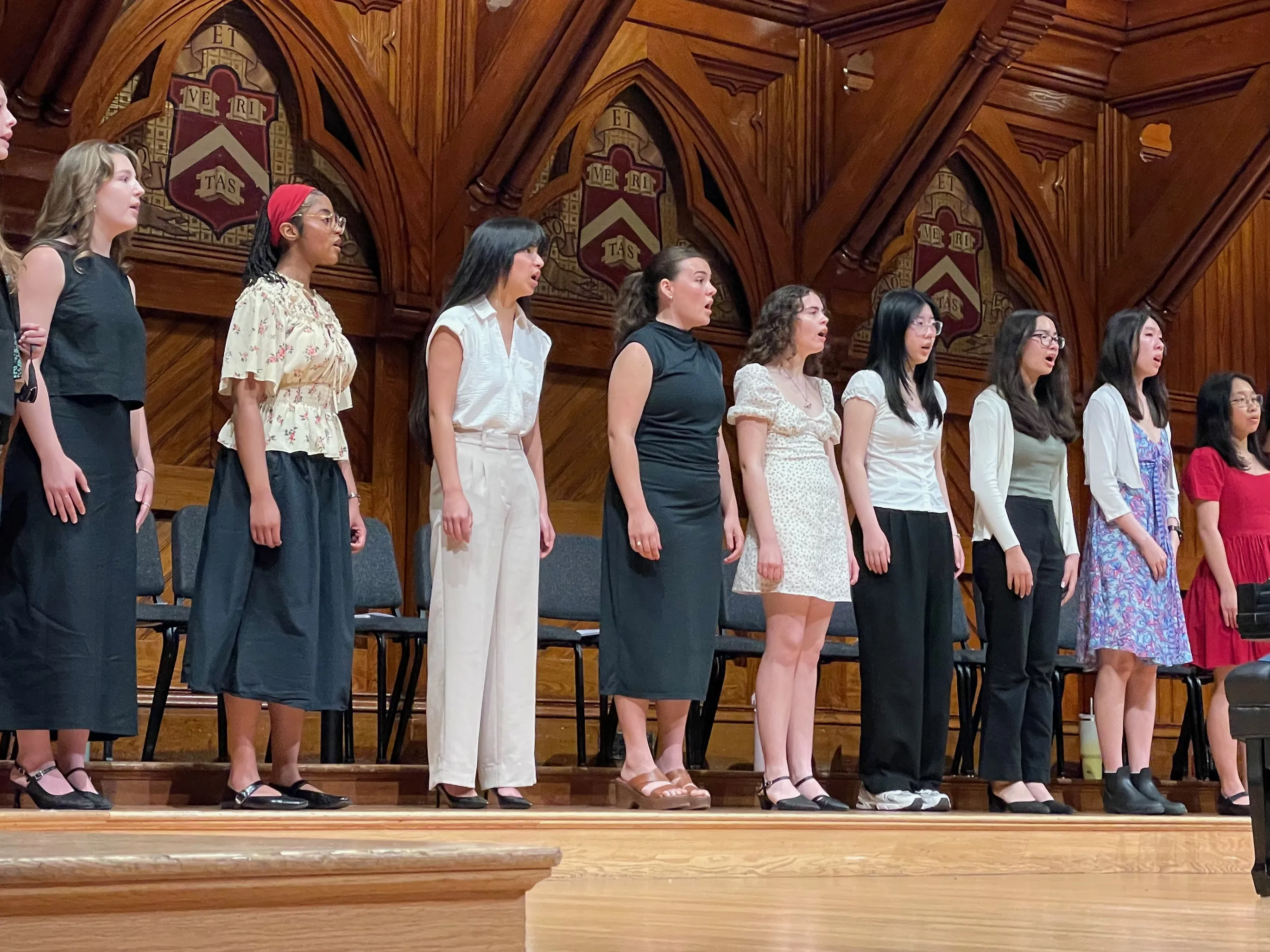 Students singing on a stage with Harvard shields in the background