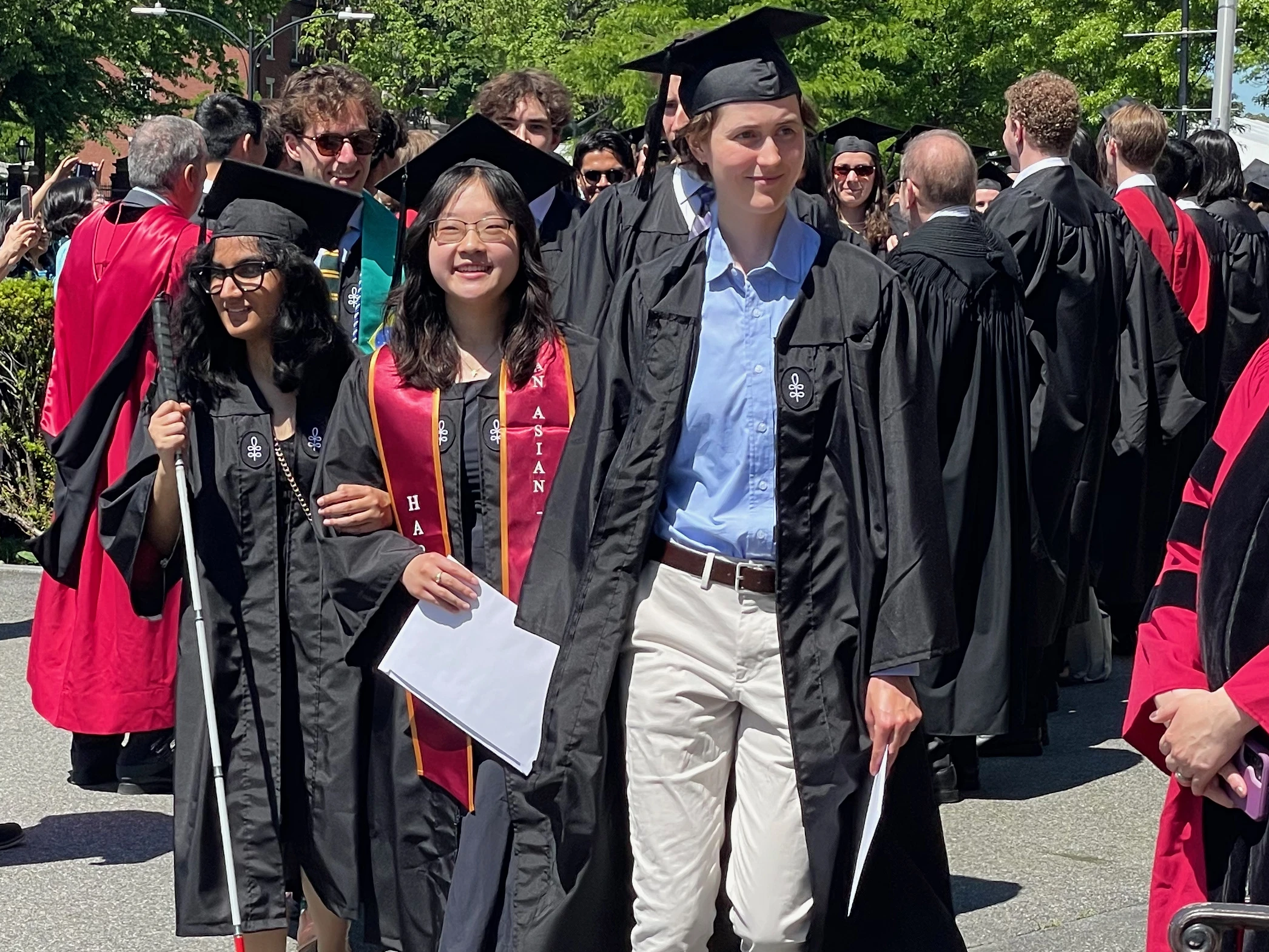 Students in black graduation caps and gowns smiling and walking