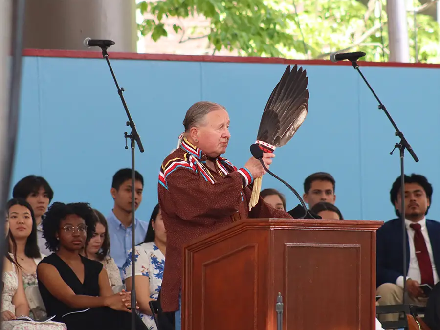 Tink Tinker waves a feather and speaks at a podium