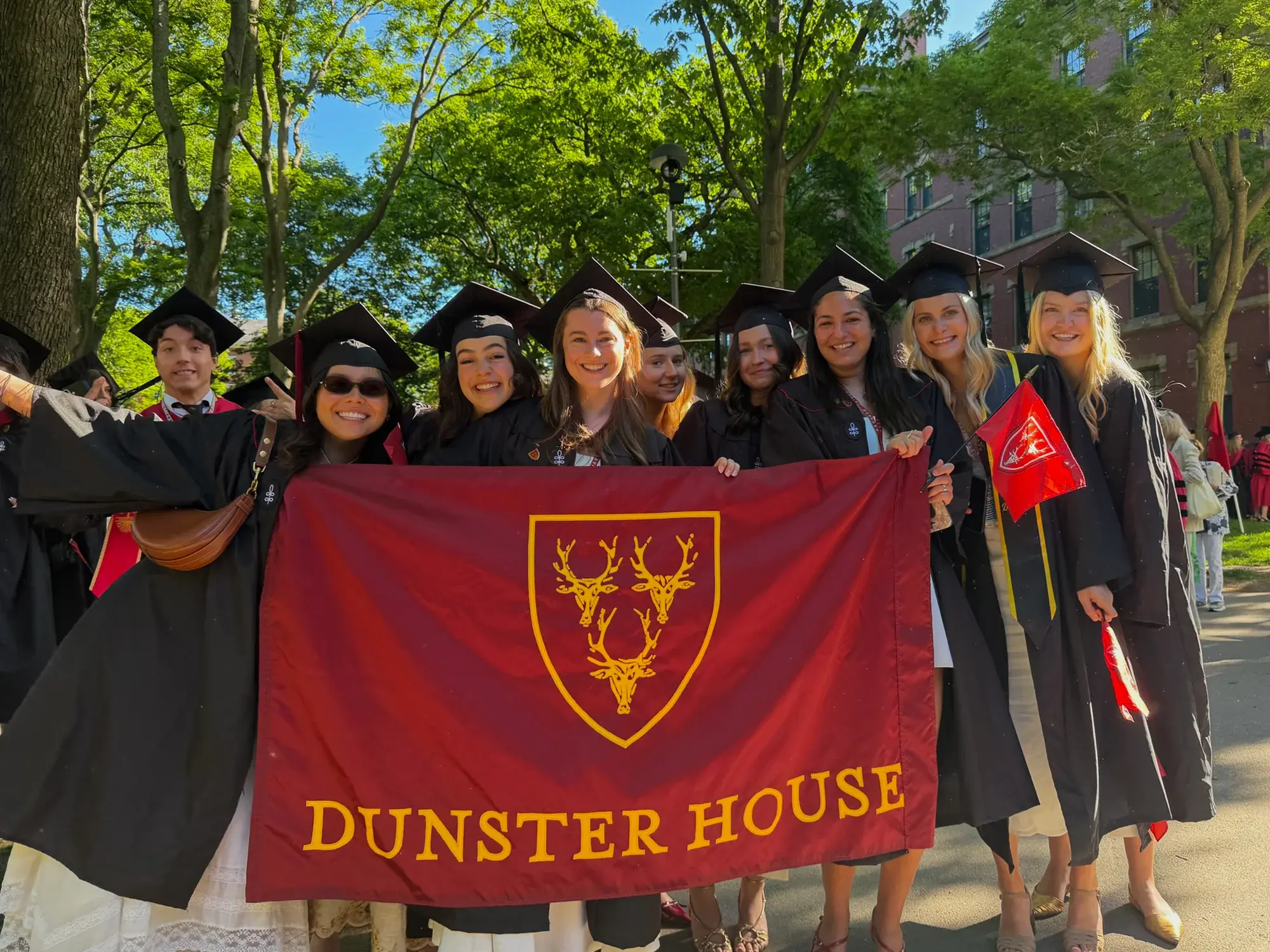 Students in black graduation cap and gown holding red banner that reads "Dunster House."