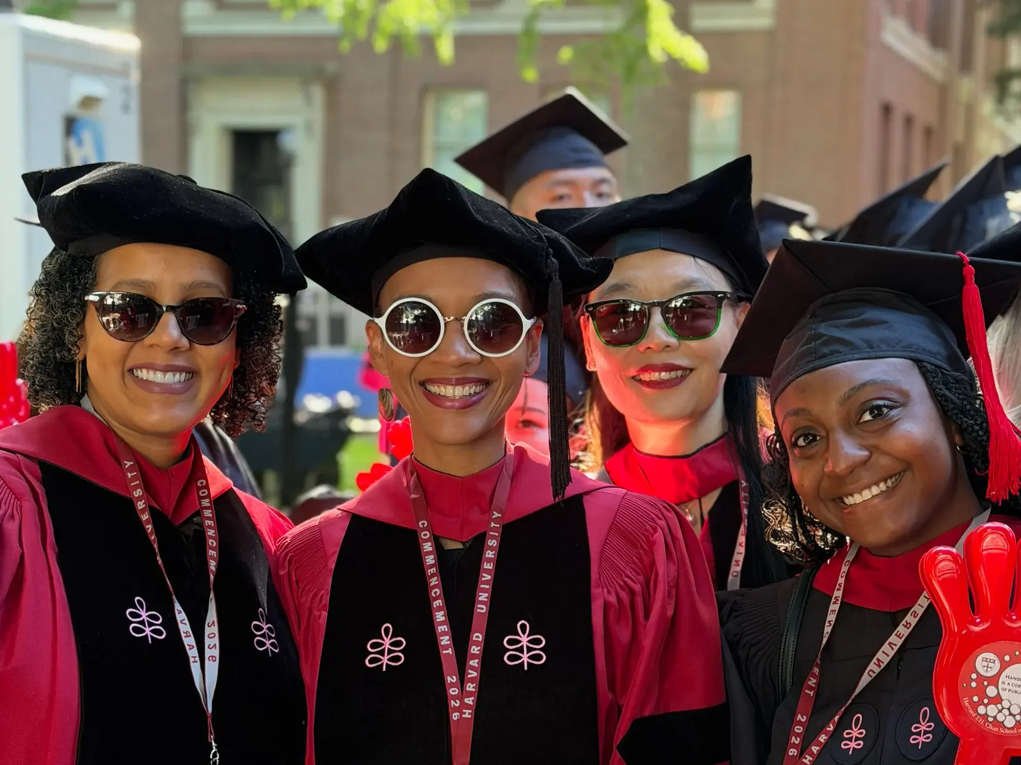 Four graduates in red and black robes with black caps and sunglasses