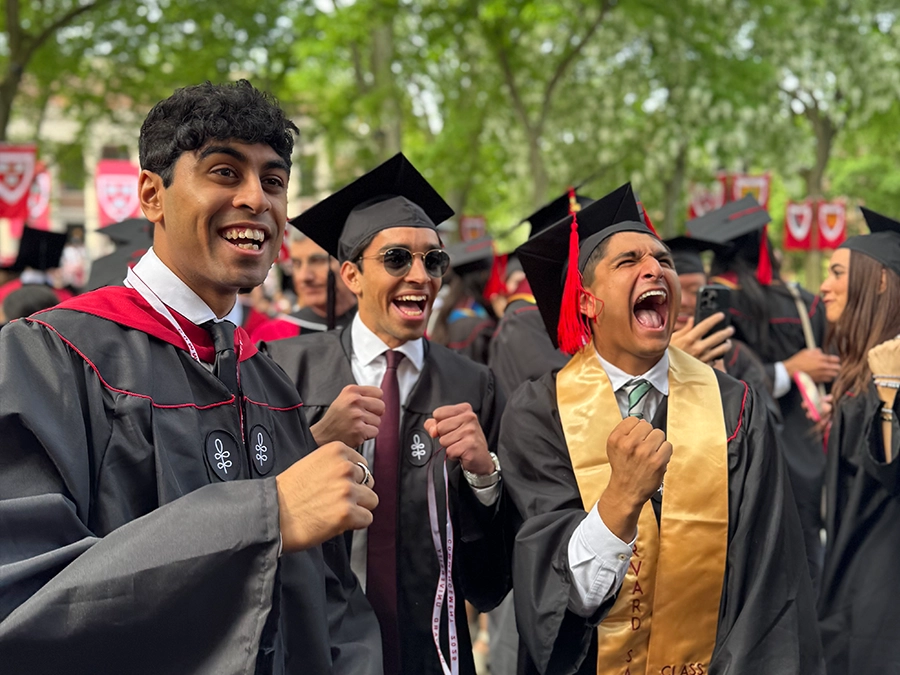 Harvard graduates in regalia with enthusiastic expressions