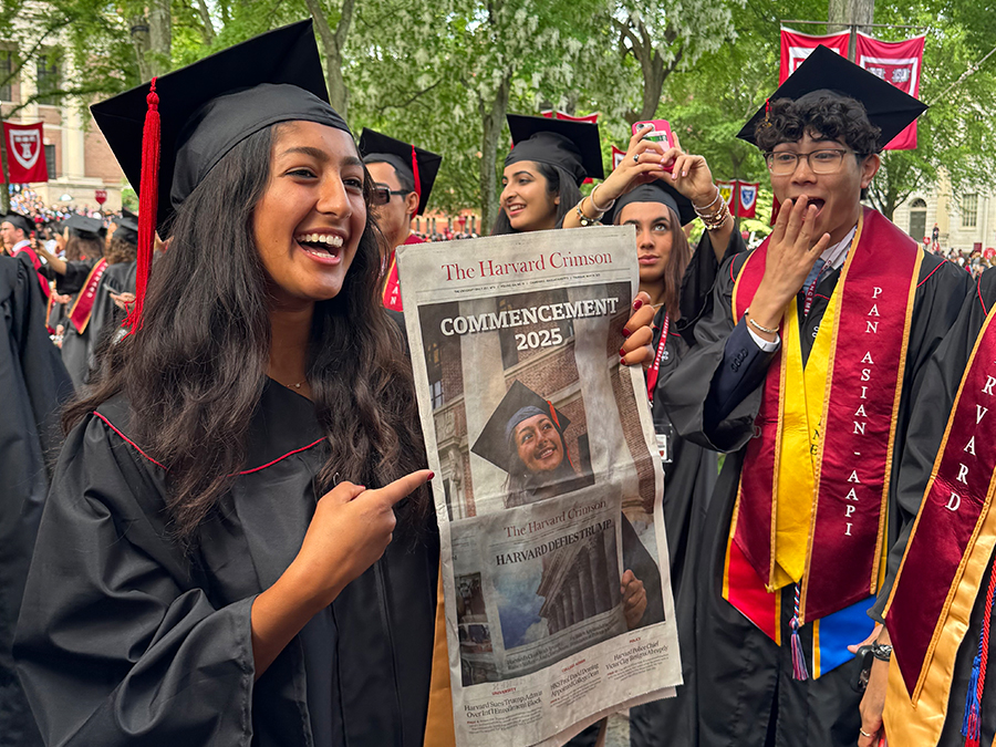 Harvard graduate holding the crimson paper