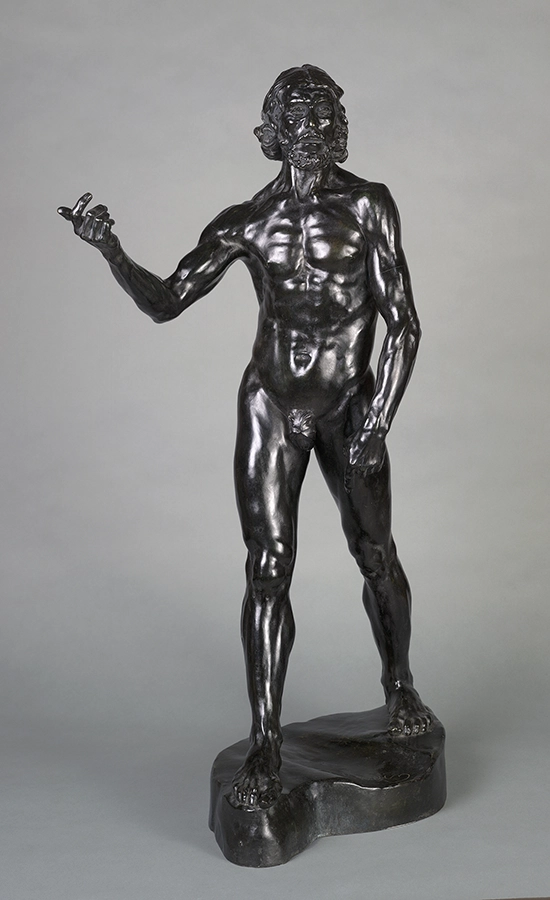 Dark bronze sculpture of a muscular, bearded nude man standing with one arm raised and hand gesturing.