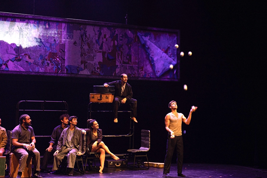 A juggler performs onstage as a group watches from bunk bed props.