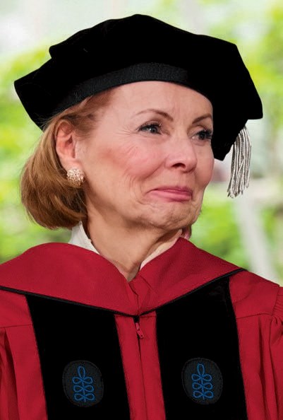 Person in red academic regalia and black doctoral cap smiles during an outdoor commencement ceremony.