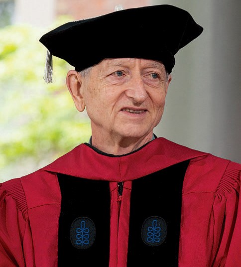 Person in red academic regalia and black doctoral cap looks ahead during commencement ceremony.
