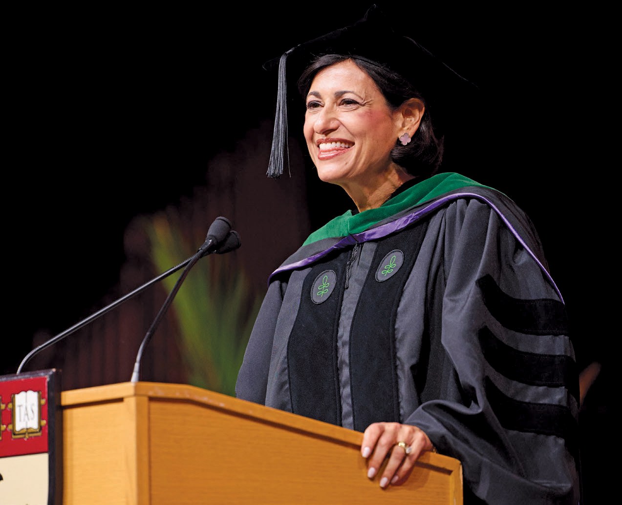 Woman in black robe and cap speaks as a podium 