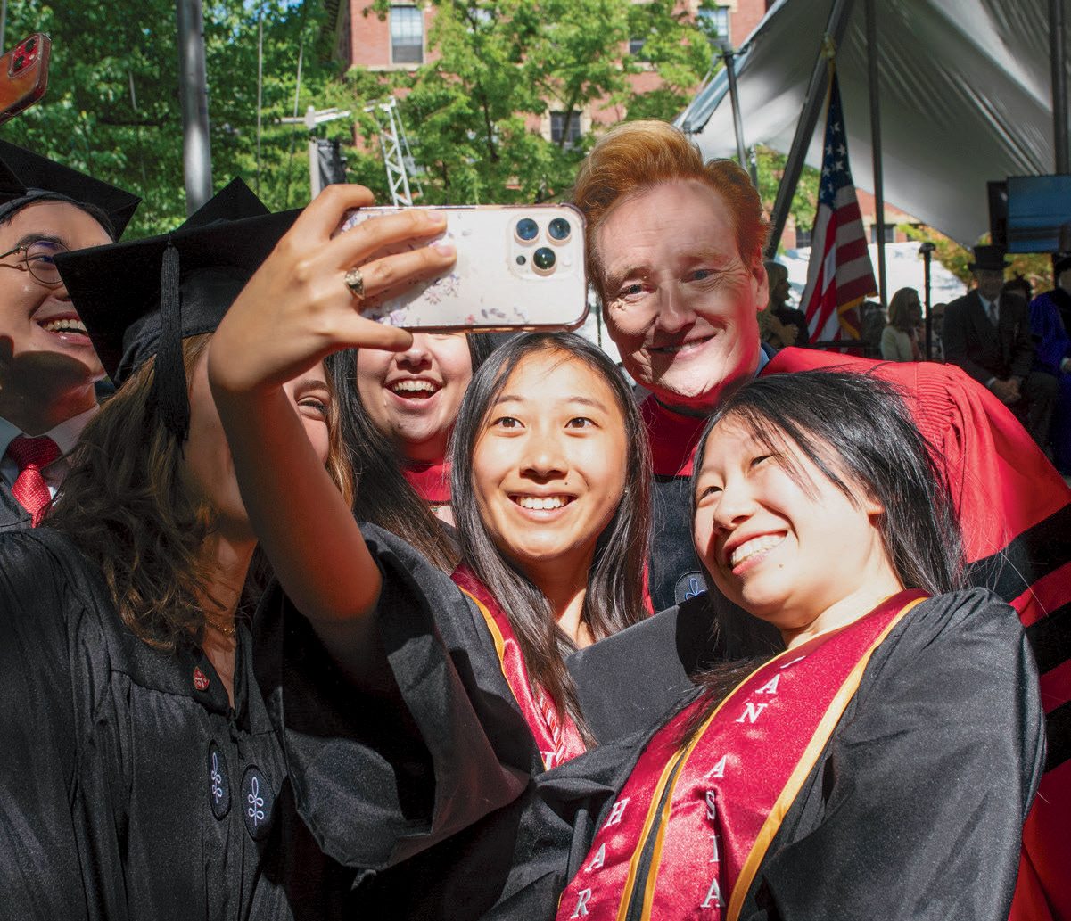 Graduates gather for a selfie with a commencement guest in academic regalia.