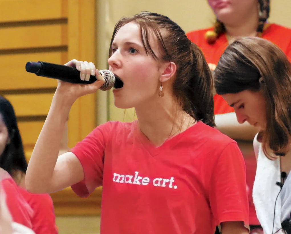 Woman in red shirt singing into a microphone.