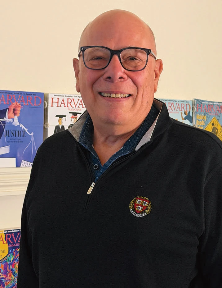 Man with glasses smiles while standing in front of a row of magazines