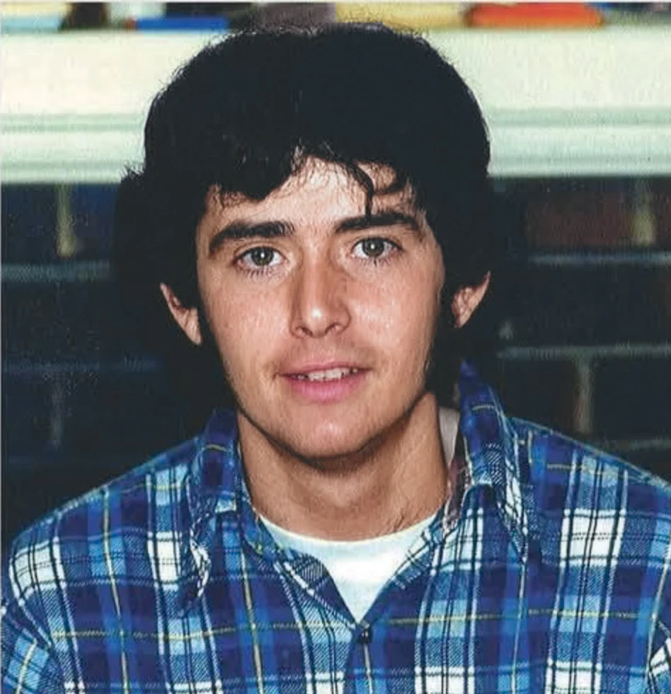 A man smiling wearing a blue plaid shirt