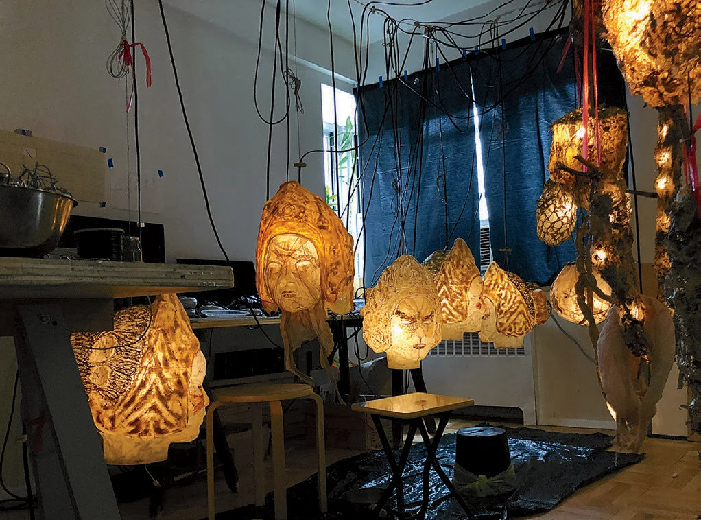 Illuminated sculptures of heads hanging from the ceiling in a small room