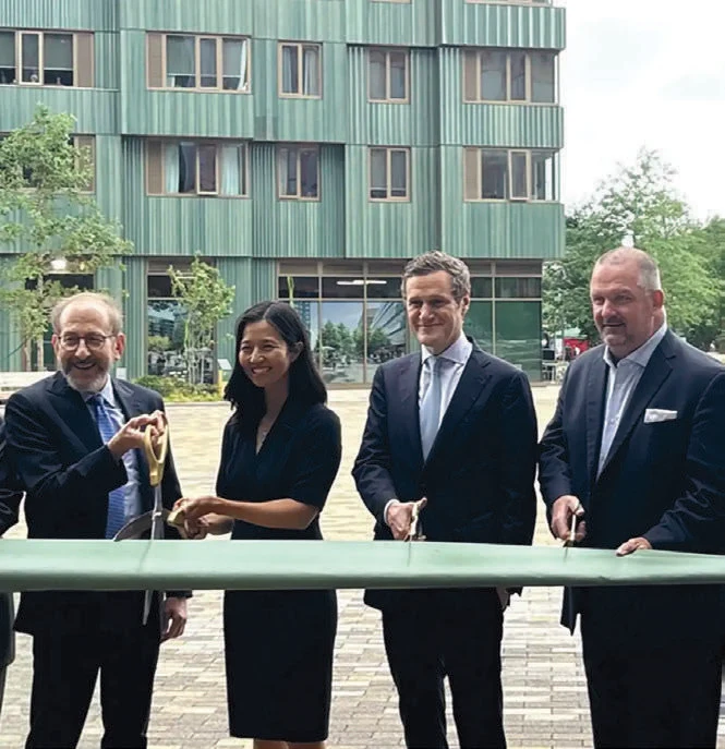 Four people stand wearing formal clothing holding scissors cutting a large ribbon in front of a building