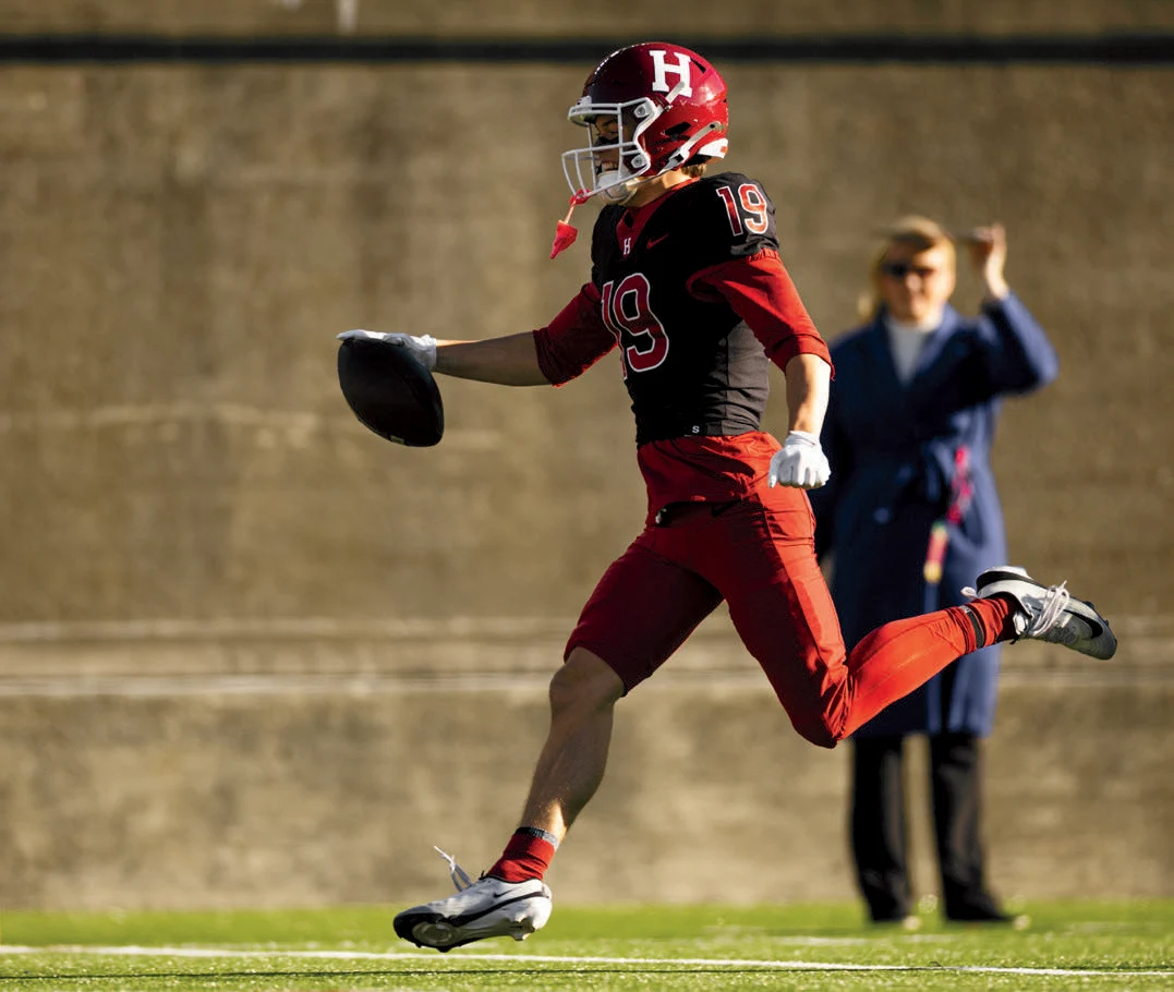 Harvard football player with #19 jersey runs with football in hand