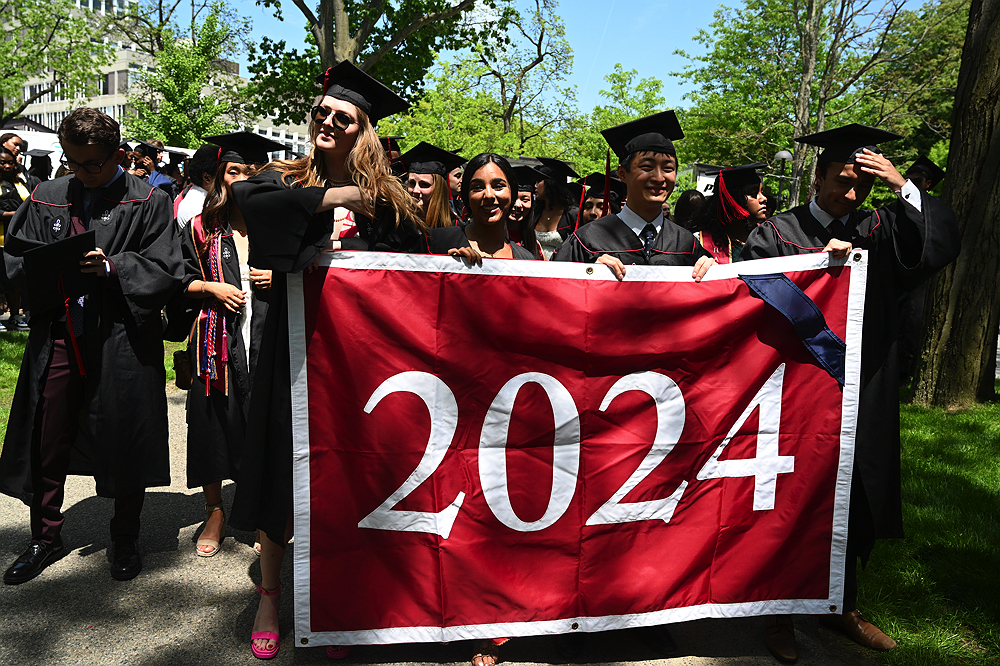 graduates in cap and gown carry the class of 2024 banner