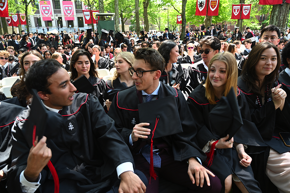 graduates in cap and gown seated outside