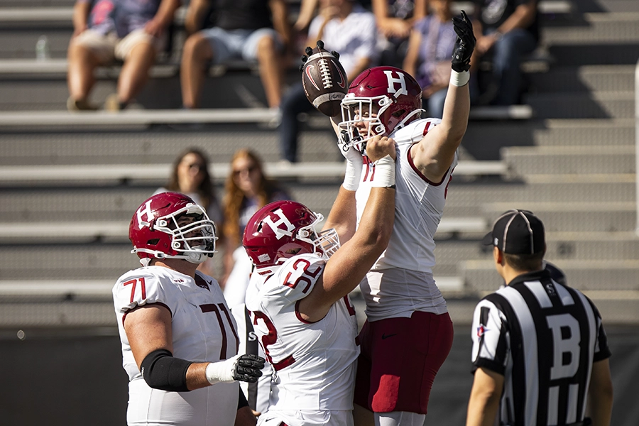 Football player lifted in celebration while holding the ball, surrounded by teammates and a referee.