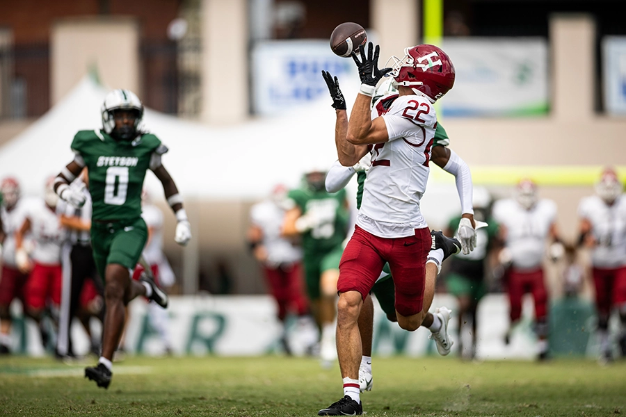 Harvard player #22 attempts a catch while being closely defended during a football game.