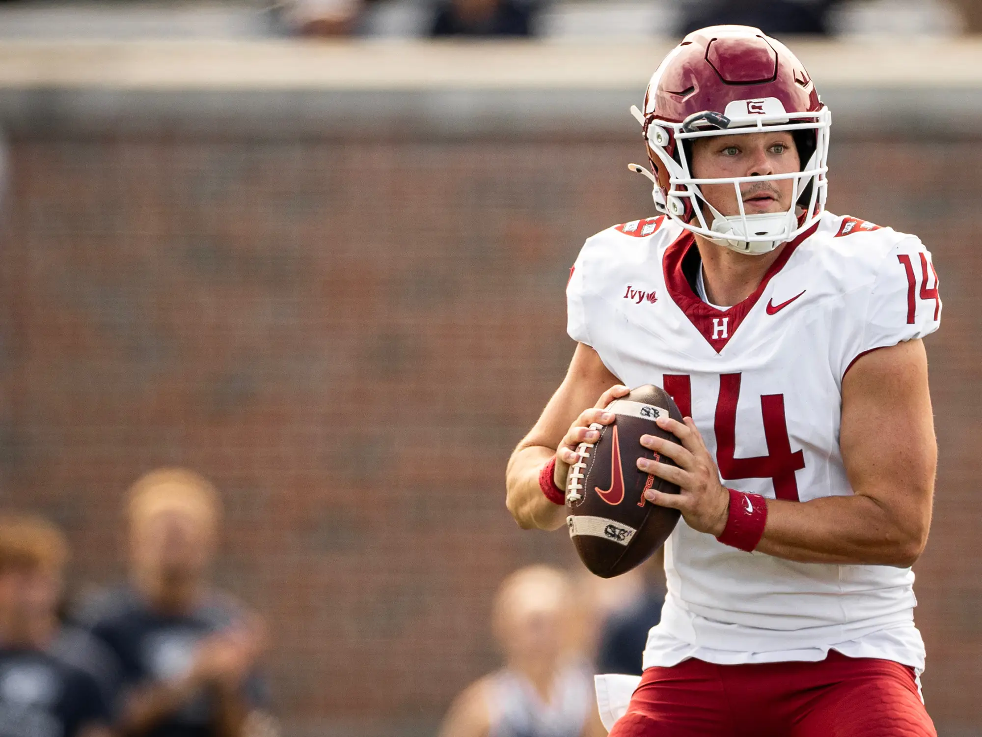Harvard football player #14 in white uniform gets ready to throw the football