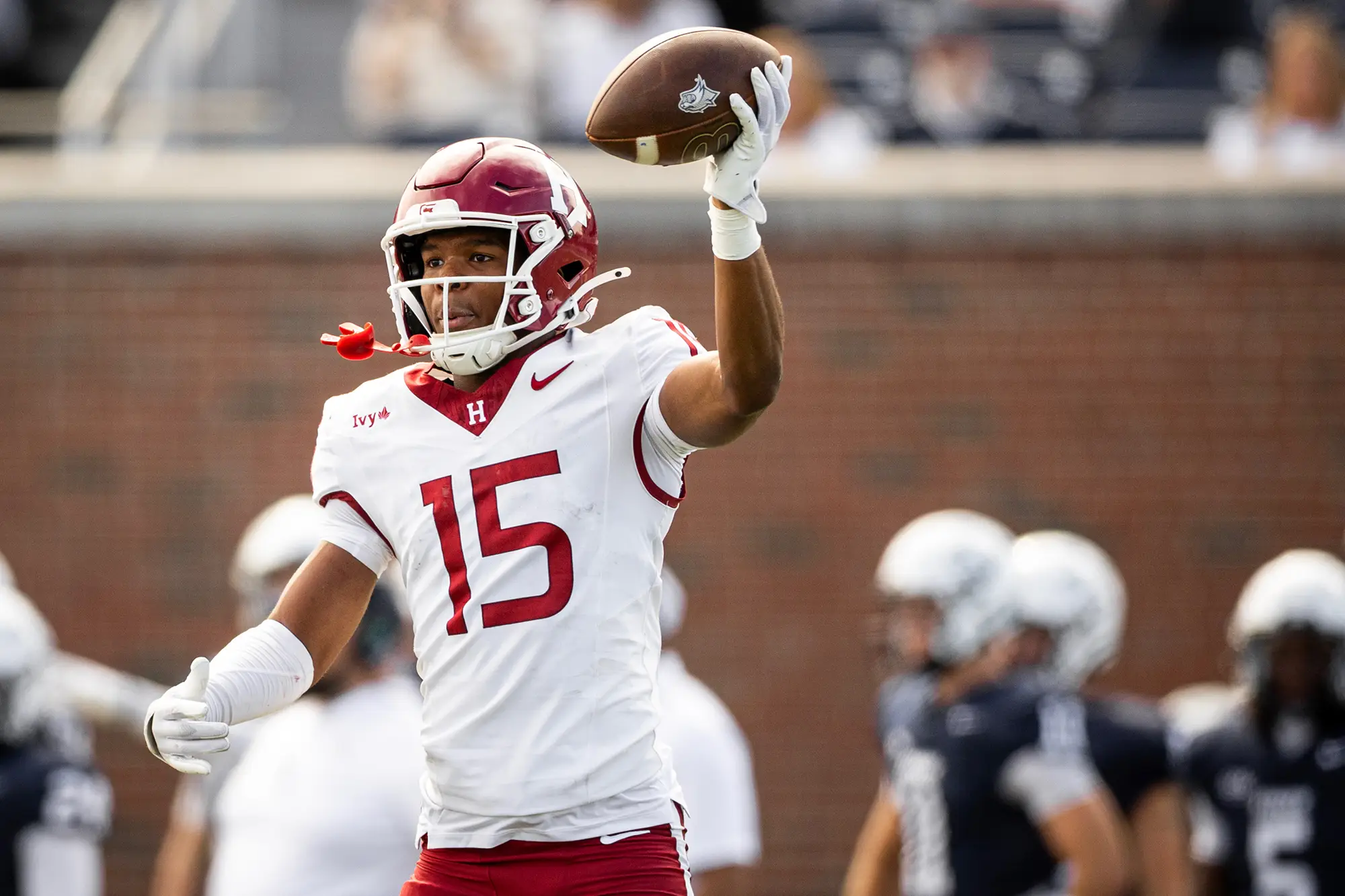Harvard football player #15 holds the football up high as he makes a touch down